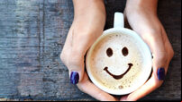 Smiley face on cappuccino foam, woman hands holding one cappuccino cup on wooden table