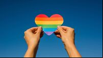 Woman holds in hands a heart in the colors of the rainbow. Young beautiful girl. LGBT history month. Pride Month. Lesbian Gay Bi