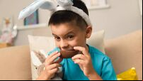 Fun brazilian child with easter bunny ears eating chocolate egg at home, in living room