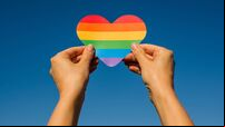 Woman holds in hands a heart in the colors of the rainbow. Young beautiful girl. LGBT history month. Pride Month. Lesbian Gay Bi