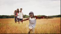 Playful boy with wings in aviators cap and flying goggles in field