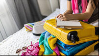 Female hands writing checklist of clothes shoes and accessories packing suitcase to travel vacation